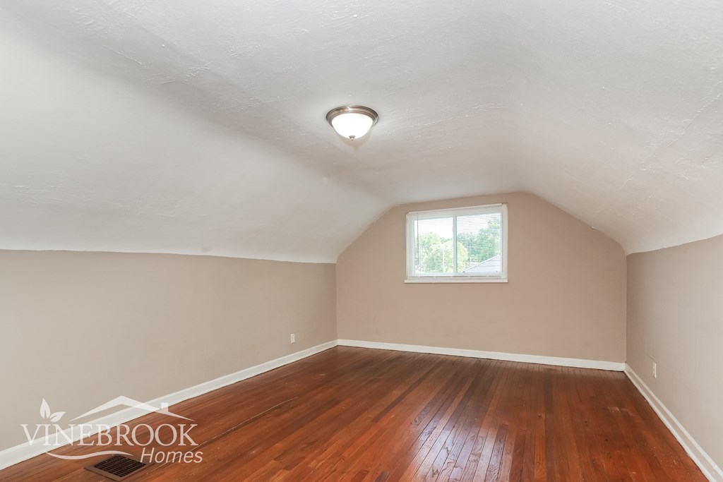 the living room of an attic with wood floors and a window