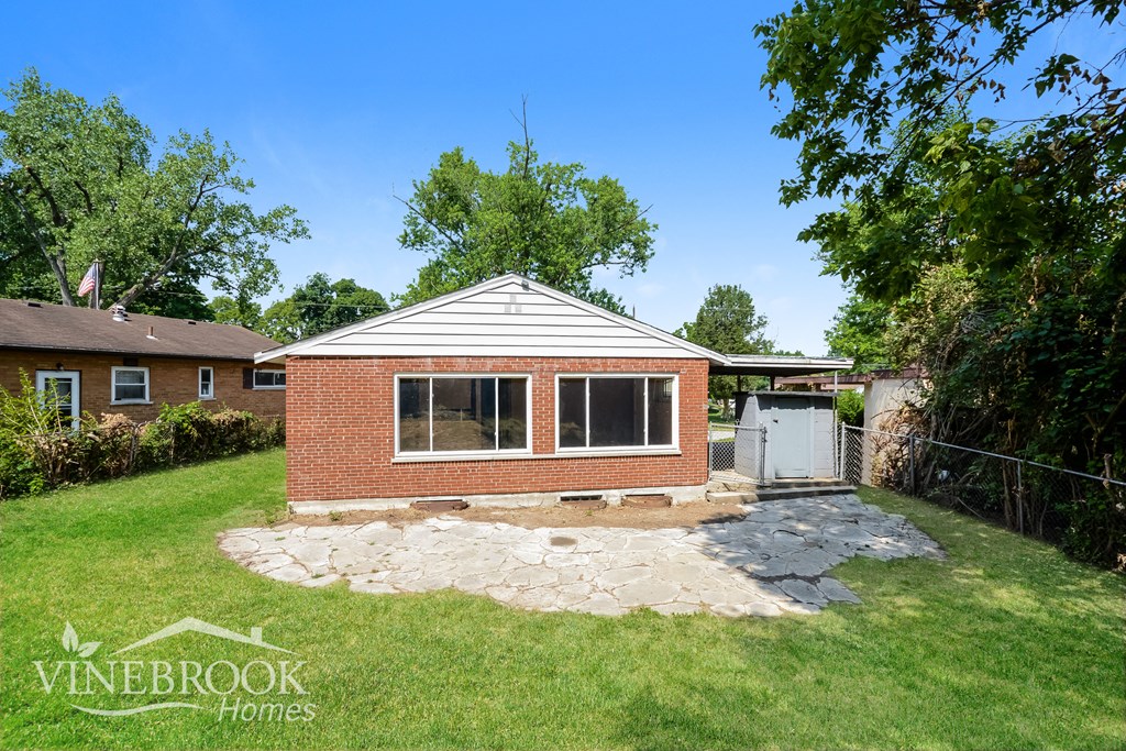the backyard of a small brick house with a stone patio