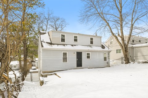 A house with a snow-covered ground and trees in the background.