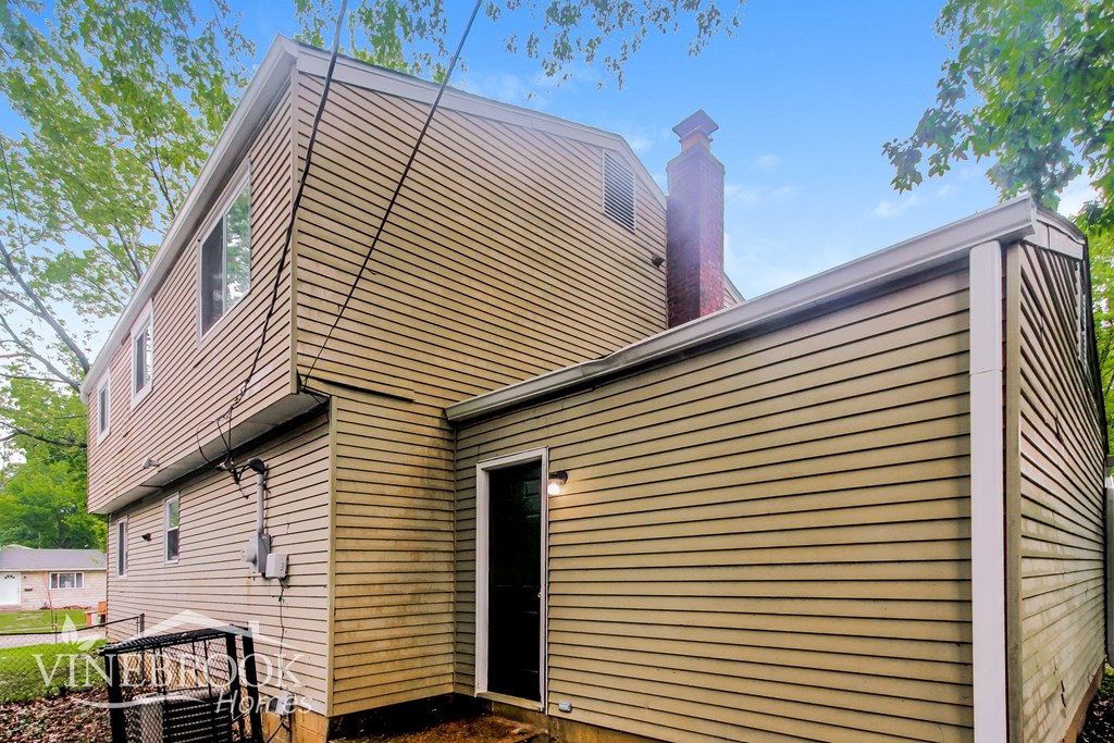 A house with a brown siding and a black door is surrounded by trees.