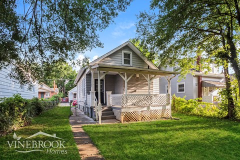 A house with a porch and a tree in front of it.