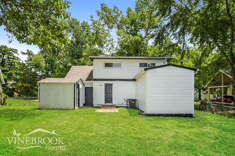 A house with a white exterior and a black door is surrounded by greenery.