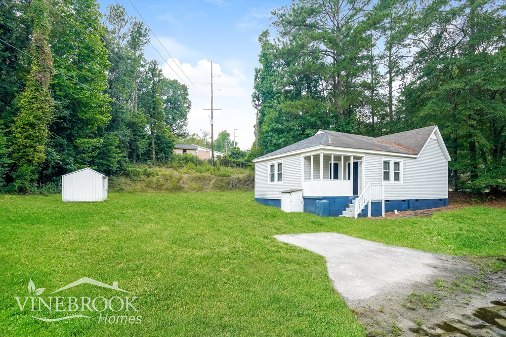 A white house with a blue trim is surrounded by greenery.