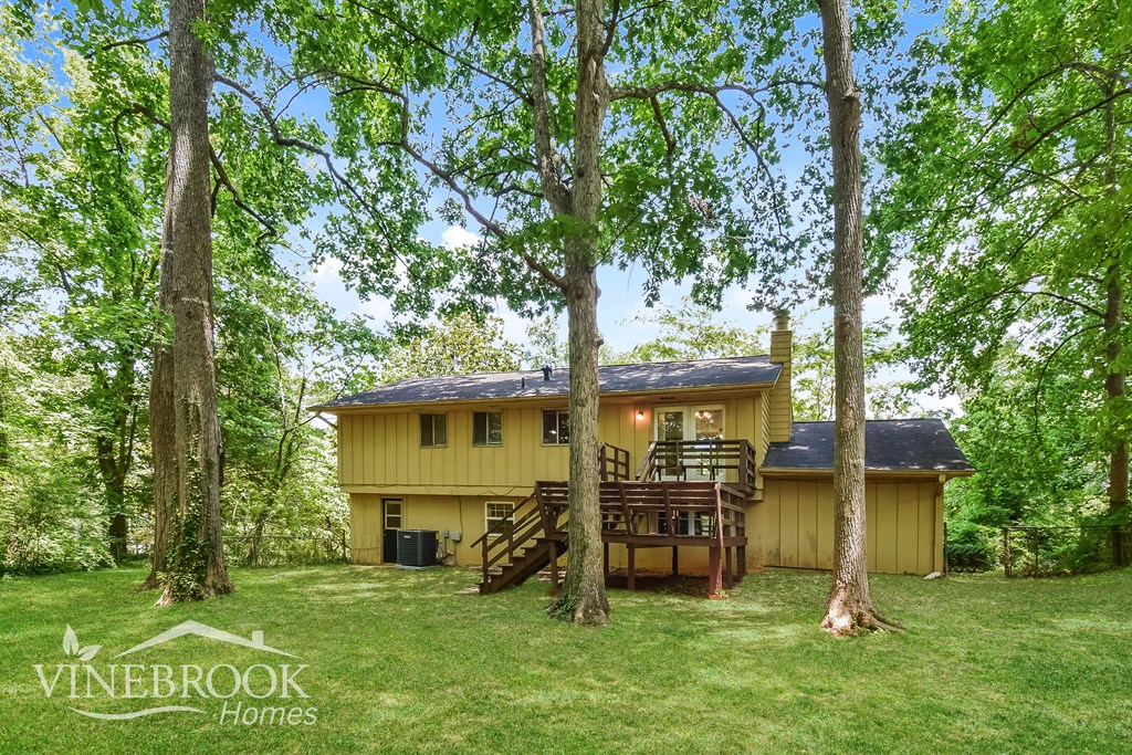 a yellow house with a deck in the woods