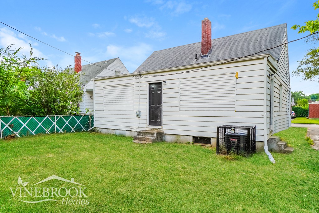 the backyard of a small white house with a lawn and a fence