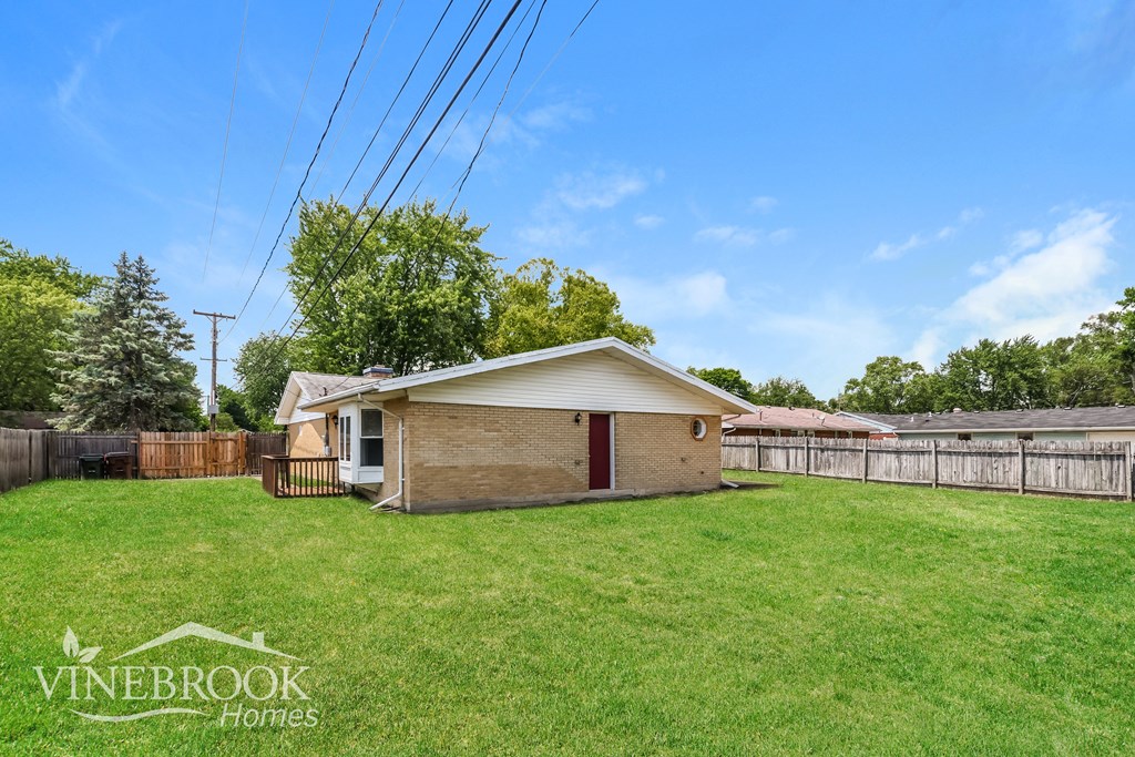 a small brick house in a grassy yard with a fence