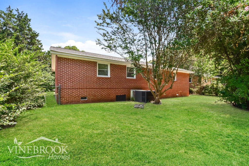 the backyard of a brick house with a lawn and trees