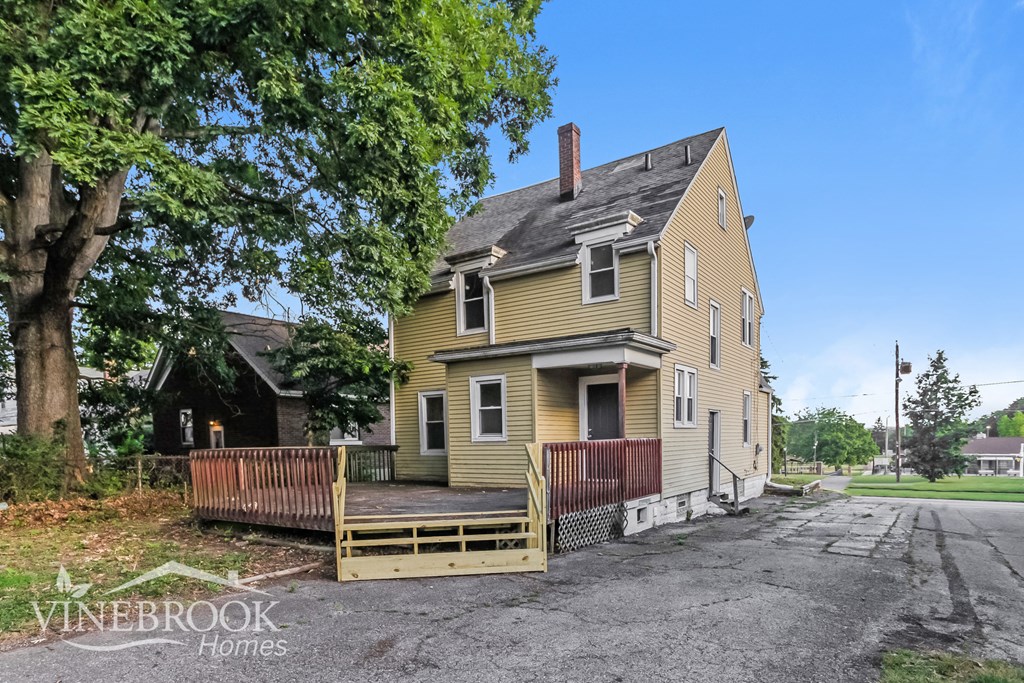 a yellow house with a wooden deck and a tree