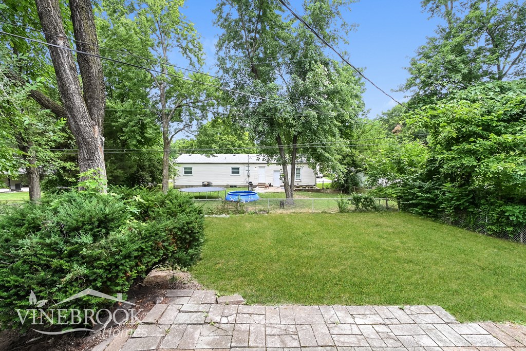 a backyard with a lawn and trees and a white house in the background