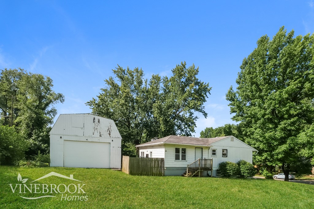 a small white house and a garage on a lawn with trees