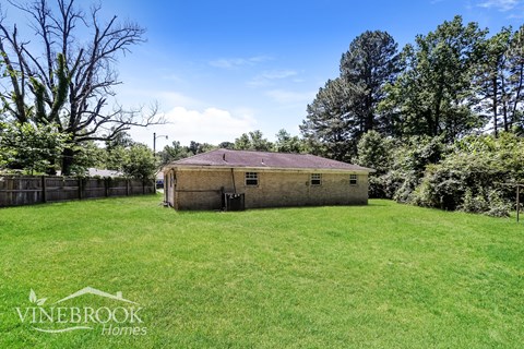 A house with a fence and trees in the background is for sale.