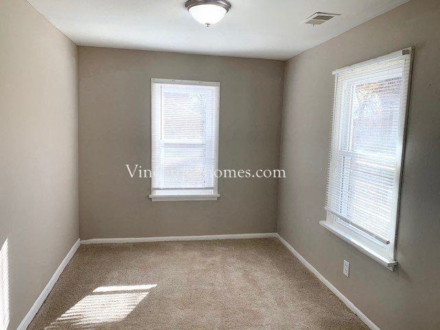 an empty room with two windows and a carpeted floor