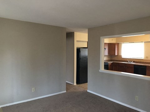 A room with a black refrigerator and a window overlooking a kitchen.