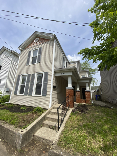 A house with a grey siding and a red brick pillar.