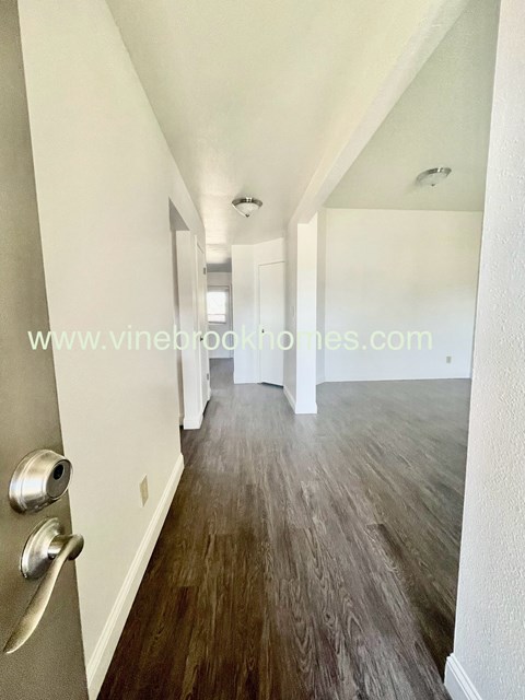 a long hallway with white walls and hardwood floors and a door with a handle