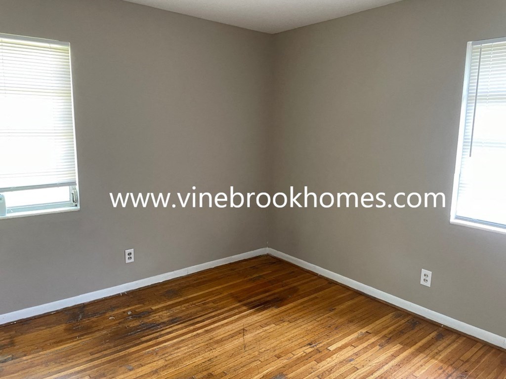 a bedroom with wood floors and grey walls and two windows