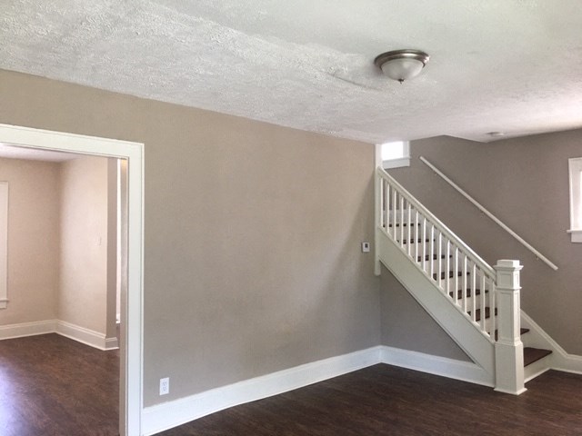 an empty living room with a staircase and a door to a hallway