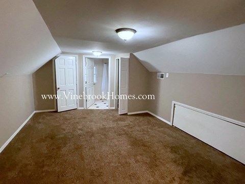 a small carpeted living room with a white wall and a ceiling lamp