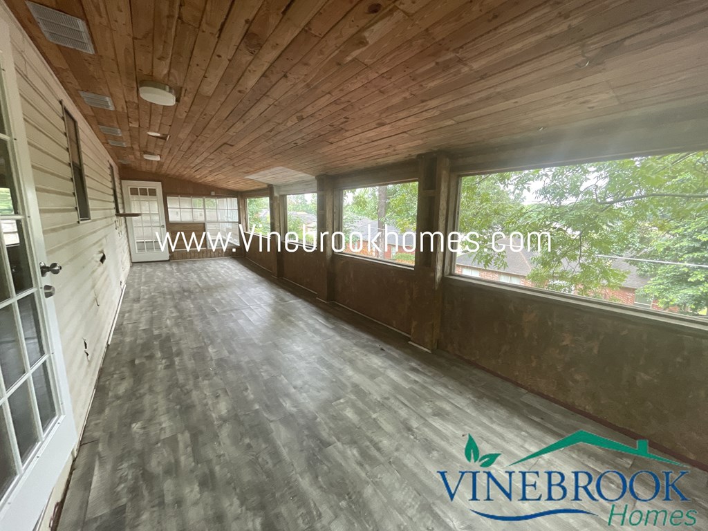 a large screened in porch with wood flooring and large windows