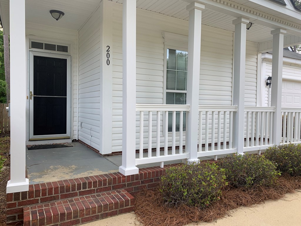 the front porch of a white house with a black door