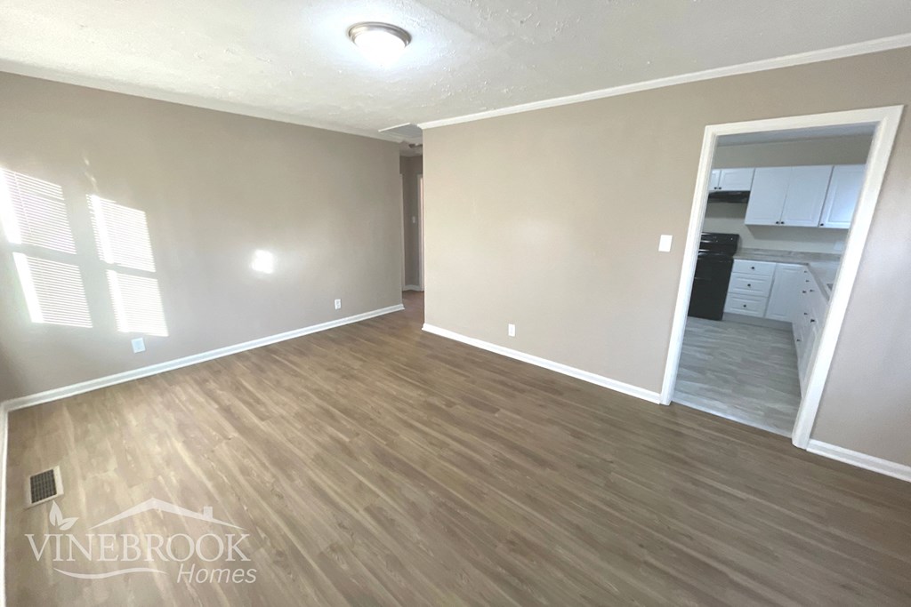 an empty living room with wood flooring and a kitchen