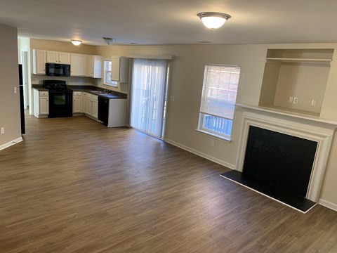 A living room with a fireplace and a kitchen area in the background.