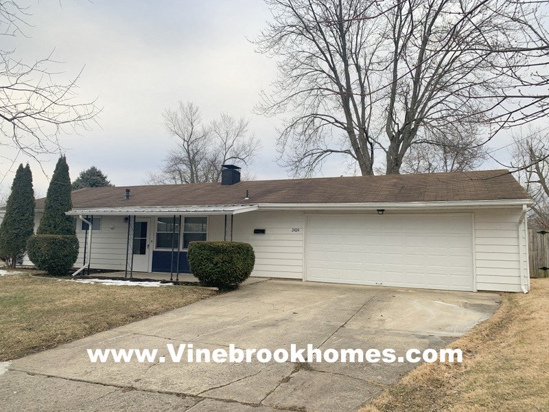 a small white house with a driveway and a tree
