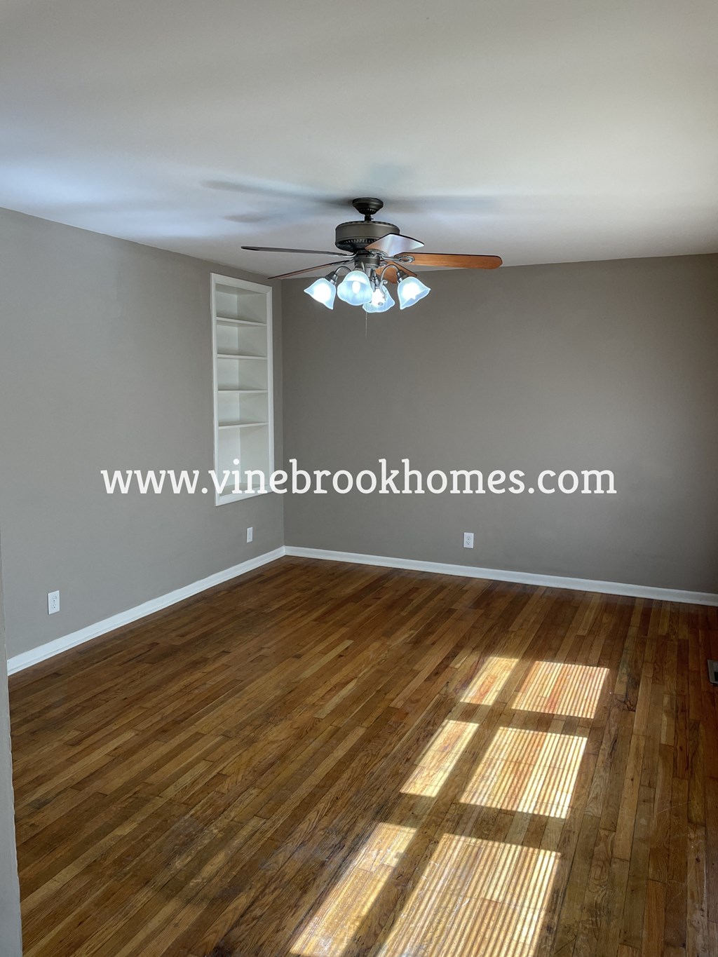 a empty living room with a ceiling fan and wood floors