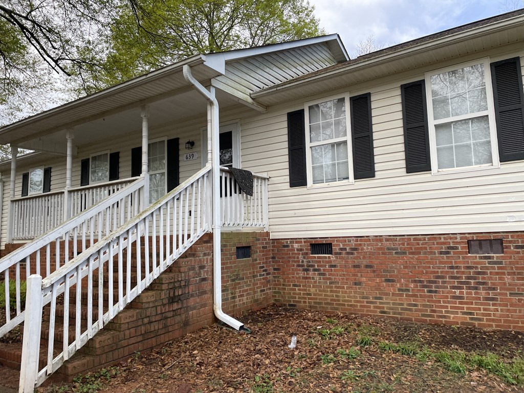the front of a house with a white porch and a brick wall