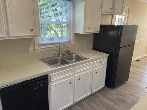 A black refrigerator sits in a kitchen with white cabinets.