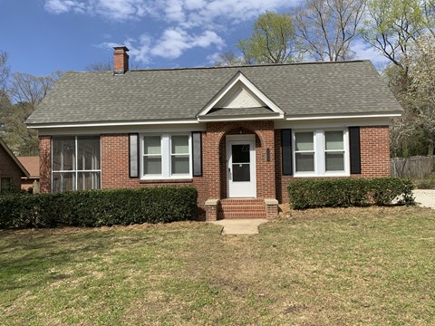 the front of a brick house with a lawn and bushes