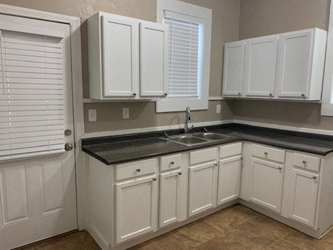 A kitchen with white cabinets and a black countertop.