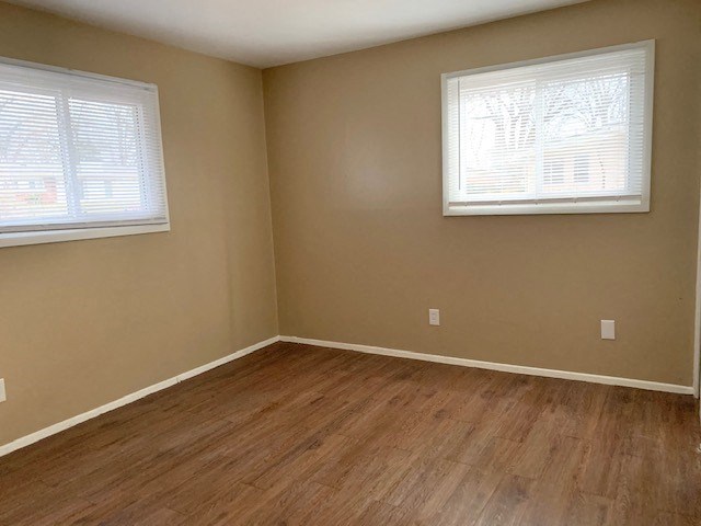 a empty room with a wooden floor and two windows
