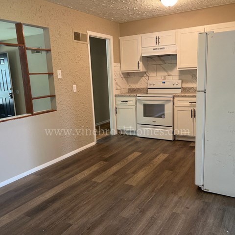 A kitchen with white appliances and wooden floors.