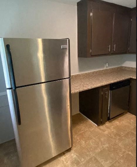 A stainless steel refrigerator stands in a kitchen with brown cabinets.