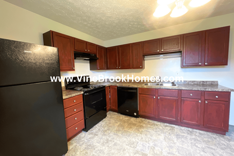 A kitchen with a black refrigerator, brown cabinets, and a stone floor.
