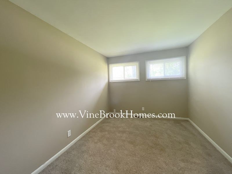 a small room with a carpet and two windows