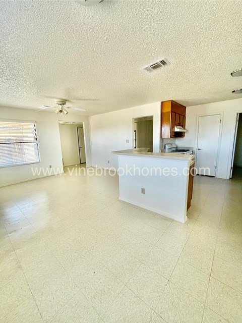 A spacious living room with a kitchen area in the background.