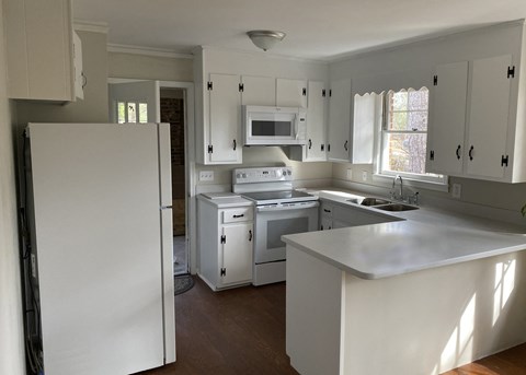 A white kitchen with a refrigerator, microwave, oven, and sink.