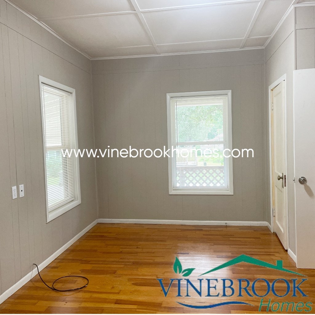 a small room with a hard wood floor and two windows