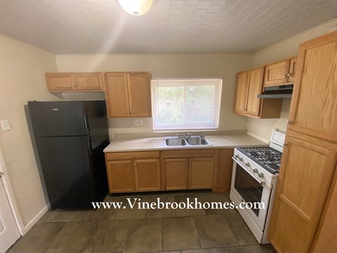 A kitchen with wooden cabinets and a black refrigerator.