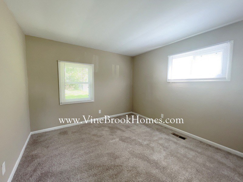 a small living room with carpet and two windows