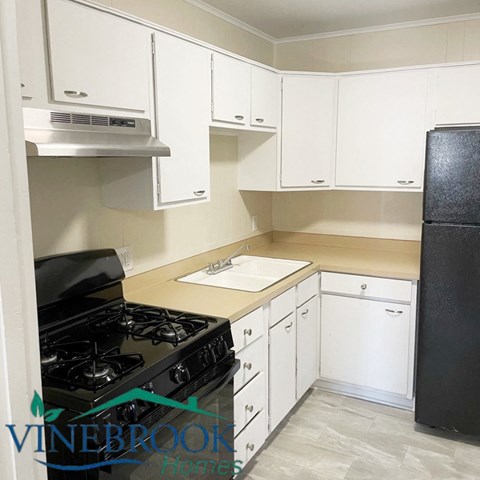 A kitchen with white cabinets and a black fridge.