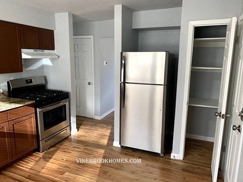 A kitchen with a stove top oven, refrigerator, and wooden floors.