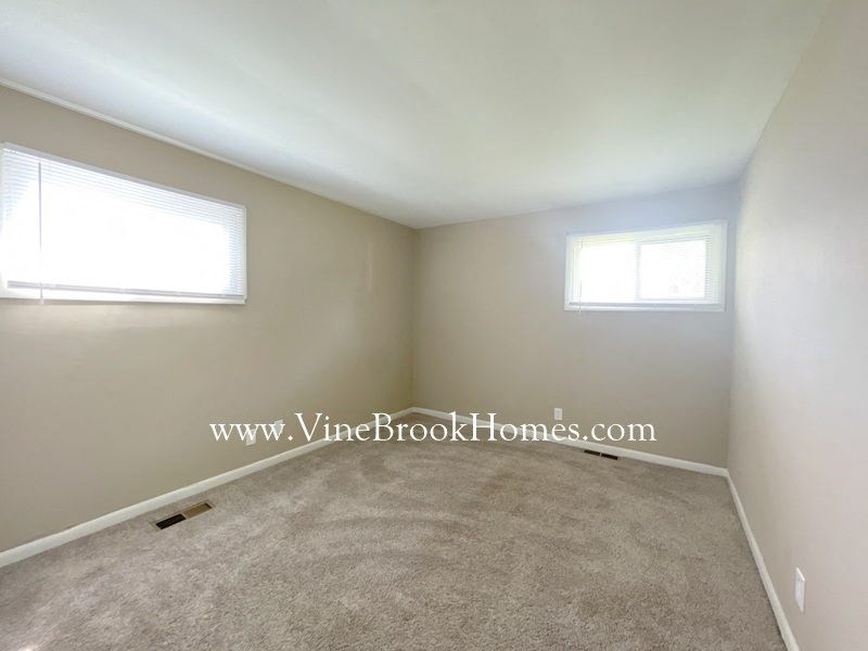 a small room with a carpet and two windows