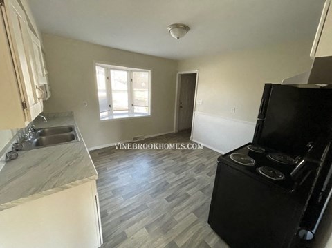 A kitchen with a black refrigerator and a window with blinds.