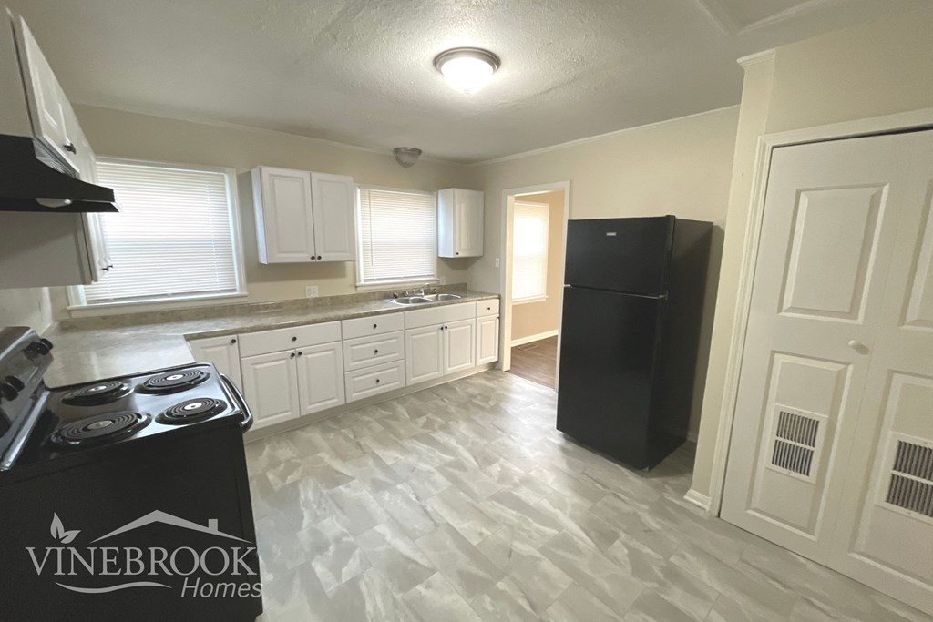 an empty kitchen with white cabinets and a black refrigerator