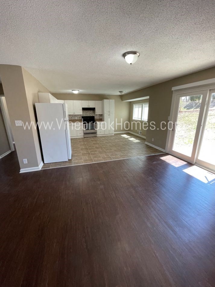 an empty living room looking into the dining room and kitchen