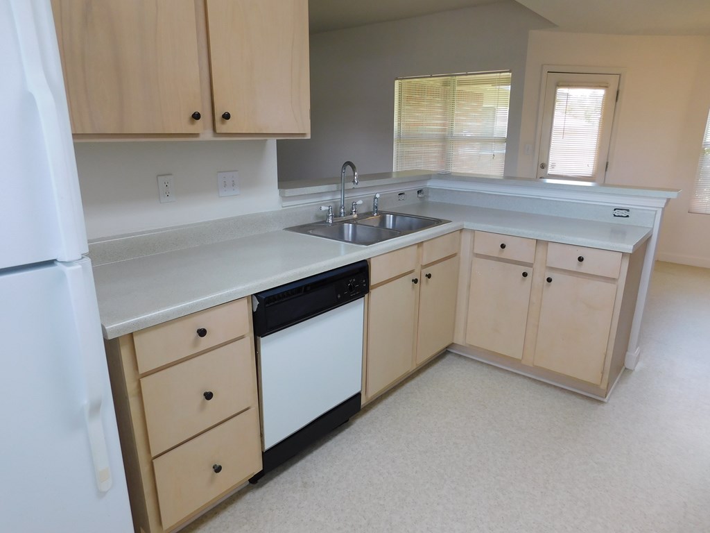 A kitchen with a white refrigerator, sink, and cabinets.