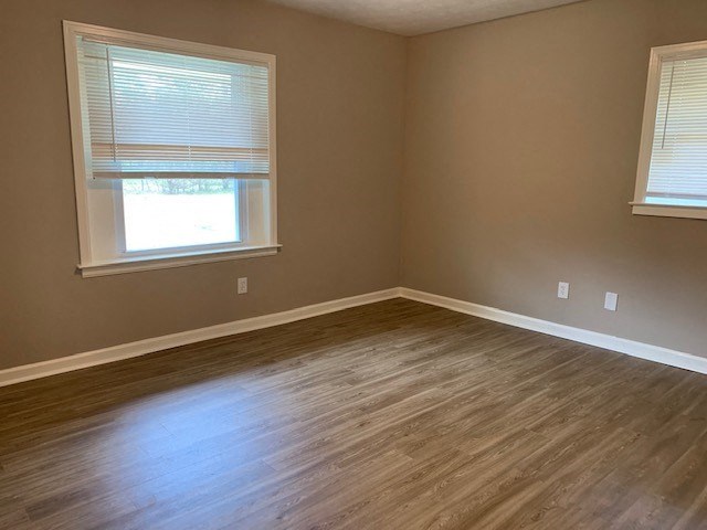 an empty room with a wooden floor and two windows
